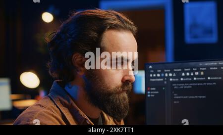 Focused software developer in home office doing coding on computer at desk, close up. IT specialist paying close attention to screen, writing lines of code at workstation, camera A Stock Photo