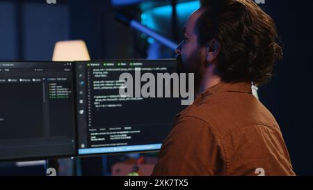 Smiling freelancing developer in home office doing coding on computer at desk. Cheerful IT expert doing contracted job from apartment, writing lines of code at workstation, camera A Stock Photo