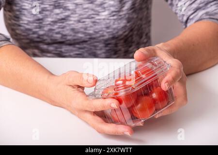Cherry tomatoes in plastic box. Woman holding small tomatoes in transparent packaging, closeup with selective focus Stock Photo