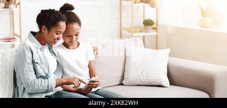 Two adorable sisters using smartphone on sofa at home Stock Photo