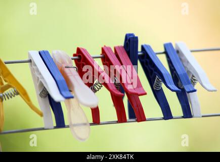 Multicoloured plastic clothes pegs hang from a clothes dryer on a green background. The metal fishing line is taut. Clothespin care. Stock Photo