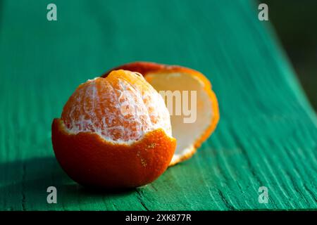 A closeup of a single peeled orange citrus clementine on a white table with the rind on the bottom of the fruit. The fresh piece of fruit is exposed Stock Photo