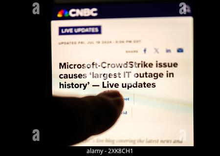 Paris, France - Jul 20, 2024: A close-up of an iPhone finger displaying a CNBC article headline Microsoft-CrowdStrike issue causes largest IT outage in history Live updates, highlighting the severity of the IT disruption Stock Photo
