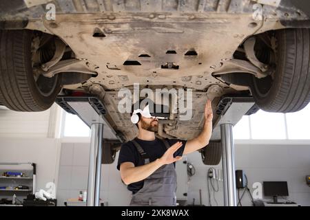 Mechanic using virtual reality to inspect car on lift Stock Photo