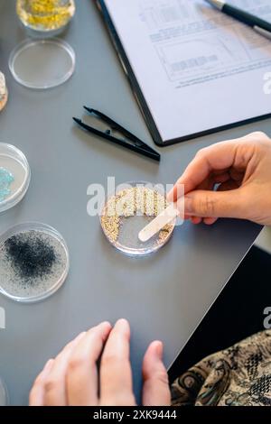 Female scientist hands taking sample of small plastic particles from glitter on petri dish in lab Stock Photo