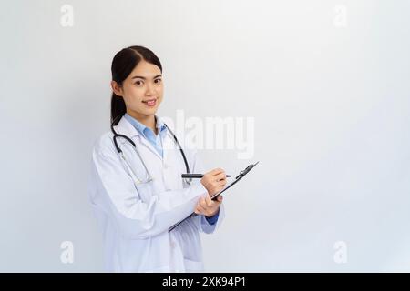 Concept of doctor and medical. Asian female Doctor hand taking note information of patient in paperwork checklist on clipboard with blue background. Stock Photo