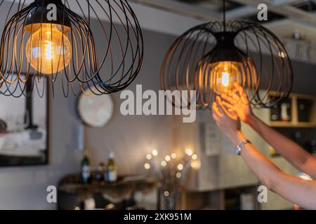 Home maintenance concept Modern interior, selective focus on light bulbs. Woman changing light bulb in hanging lamp at home The homeowner cleans or re Stock Photo