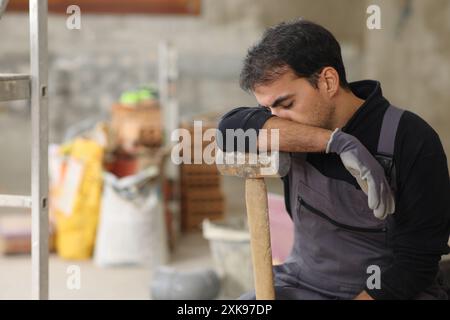 Tired construction worker resting leaning on hammer in a house under renovation Stock Photo