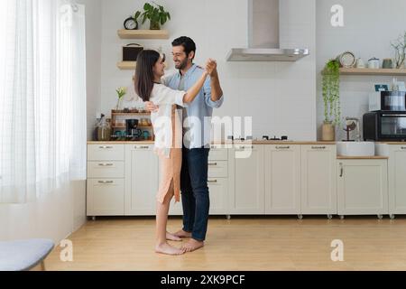 Beautiful young couple dancing in kitchen at home. Happy loving young couple dancing on date in modern kitchen smiling husband and wife celebrating an Stock Photo