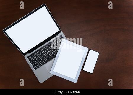 Laptops, tablets and smartphones with blank screens on table, devices are highly used in communication technology these days. Flat top view with copy Stock Photo
