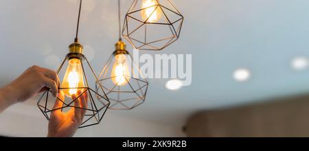An electrician is installing spotlights on the ceiling. Handyman choosing between energy save and cheap incandescent lamp while changing light in the Stock Photo