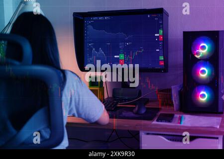 Back view of female trader looking at monitor with stock exchange graph or chart.Centennial young person seen from behind buying and selling cryptocur Stock Photo