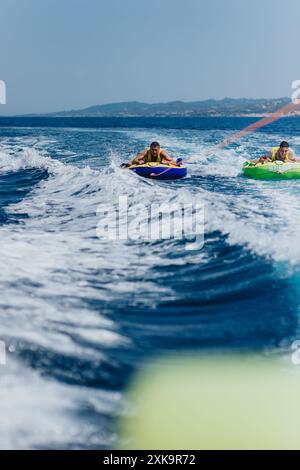 Two friends enjoying summer speedboat tubing on the sea with mountains in the background Stock Photo