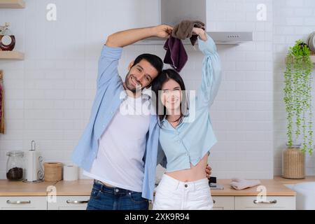 Young family couple doing cleaning in the house. Cleaning concept. Cheerful young european lady and male washing dishes in modern kitchen interior. Hy Stock Photo