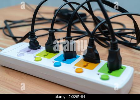 Socket strip and connected plugs on background. Many plugs connected to the power strip with individual switches. Surge protector with connected white Stock Photo