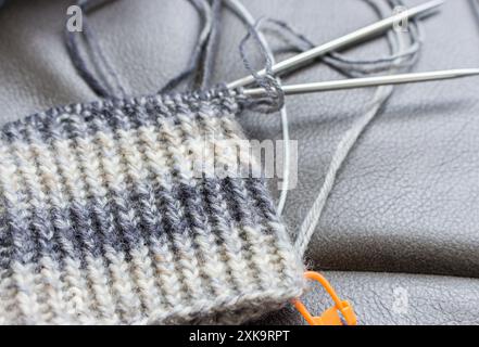 Knitting needles and crochet with orange marker. Knitting hobby. Striped pattern of wool yarn and knitting needles. Retro still life. Needlework art. Stock Photo