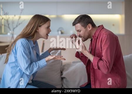 Sign language debate. Romantic couple sits on couch, gesturing actively, arguing using sign language Stock Photo