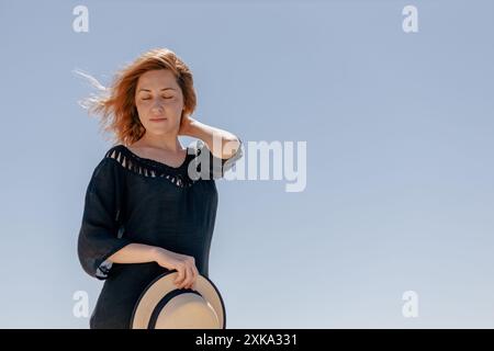 Stylish woman in dress holding straw hat on blue sky Stock Photo