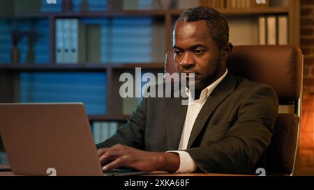 Adult african american businessman working on laptop in office unhealthy tired man suffering from headache feels pain pressure fatigue from overwork Stock Photo