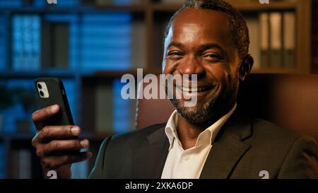 Focused businessman sitting in office holding smartphone browsing email on phone chatting with client in internet using mobile app confident happy Stock Photo