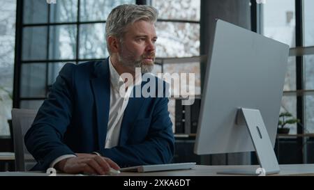 Mature focused thoughtful caucasian businessman marketing specialist working on computer in office man entrepreneur manager thinking analyzing finance Stock Photo