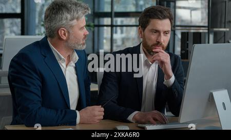 Mature businessman mentoring man discussing project on computer consulting investor client about digital investment in office Caucasian businessmen Stock Photo