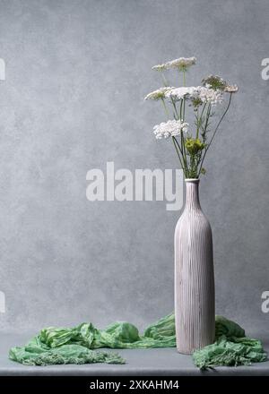 Still life with flowers. White wildflowers in a light tall vase on a light gray background. Congratulations, postcard. Plenty of room for text Stock Photo