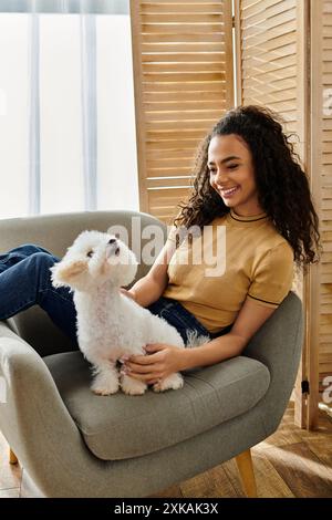 A young woman sitting on a chair with her white Bichon Frise dog. Stock Photo