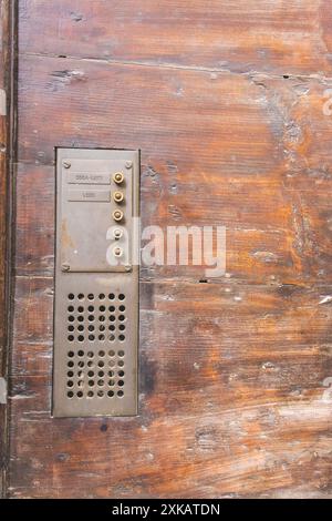 A rustic, rusty intercom doorbell system for flats and apartments on a wooden door at the entrance to a building in Citta Alta in Bergamo, Italy. Stock Photo