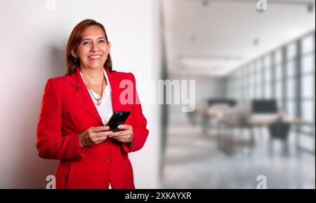 business concepts. beautiful businesswoman in red coat smiles while holding a smart phone in her hands. empowered woman successfully runs company Stock Photo