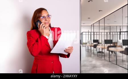 business concepts. beautiful businesswoman in red coat smiles while holding important documents in her hands. empowered woman runs company successfull Stock Photo
