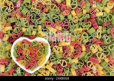 Italian tricolor uncooked Italian pasta food background with heart shape dish and easter symbols of eggs,rabbits & tulip flowers in red green, yellow. Stock Photo