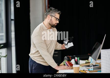 A handsome businessman with a beard examines a virtual reality headset while working in his modern office. Stock Photo