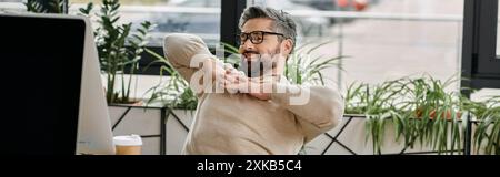 A handsome businessman with a beard stretches in a modern office, taking a break from work. Stock Photo