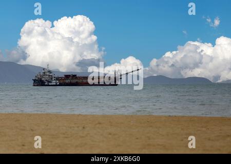 A sand suction boat is working in the middle of the sea, in the background is a sky with white clouds. Stock Photo