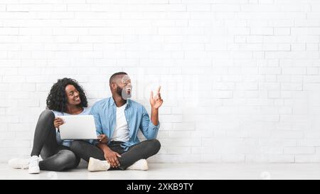 Young couple with laptop pointing at empty space Stock Photo