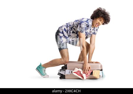 Angry young man trying to close overpacked suitcase isolated on white background Stock Photo