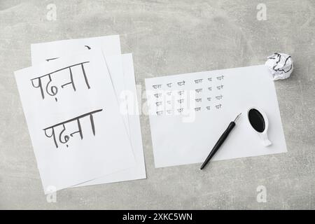Calligraphy. Sheets of paper with written words Reading and Read in Hindi, inkwell and fountain pen on grey background, top view Stock Photo
