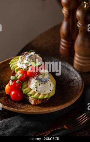 Slice of bread with avocado sliced, tomatoes and poached eggs on top. Restaurant table. Sourdough toast. Stock Photo