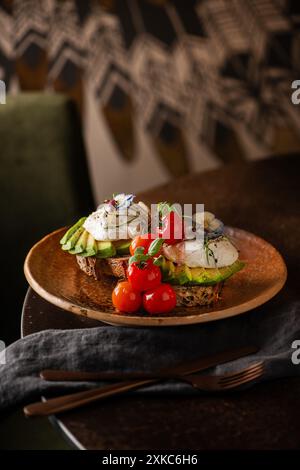 Slice of bread with avocado sliced, tomatoes and poached eggs on top. Restaurant table. Sourdough toast. Stock Photo