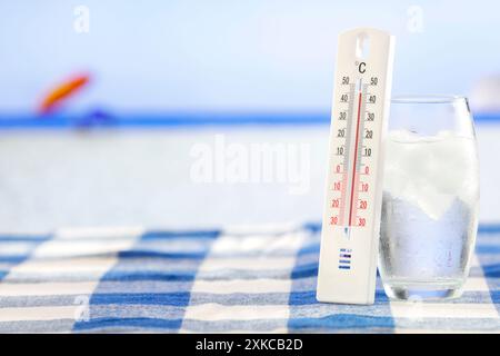 Glass with cold water with ice cubes and thermometer and beach and sea background. Summer cool drink on hot days. Copy space for products. Stock Photo