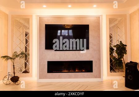 A modern living room with evening lighting, featuring a wall-mounted TV, an elegant fireplace, and ceiling LED lights. Stock Photo