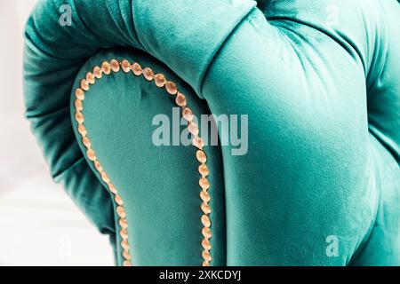 Close-up view of a turquoise velvet sofa armrest adorned with gold studs, highlighting its luxurious design and texture. Stock Photo