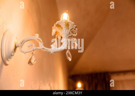A close-up of an ornate wall sconce emitting a warm glow with decorative crystals hanging from it. Stock Photo