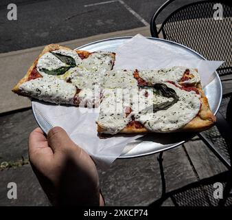 two square slices of sicilian style pizza (fresh white mozzarella basil leaves thin crust) on round tray with parchment paper (italian food) red peppe Stock Photo