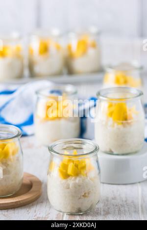 Coconut rice pudding with mango in dessert glasses on white wooden background, vertical Stock Photo