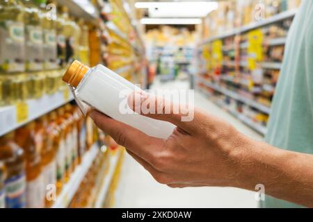 Man chooses natural organic coconut oil in glass bottle in a grocery supermarket aisle standing at the shelves with products. Male reading label on Stock Photo