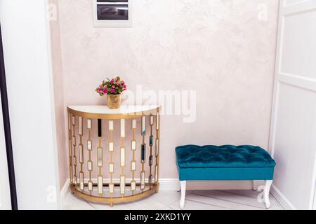 A stylish corner featuring a semi-circular console table with a vase of flowers, and a plush turquoise bench against a textured wall. Stock Photo