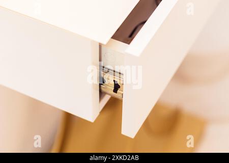 A close-up view of an open white console table drawer showcasing the metal sliding mechanism. Stock Photo