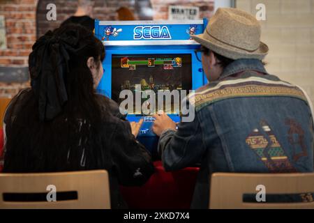 HARROGATE, UK - JUNE 22, 2024. Rear view of two friends playing against each other on a retro SEGA arcade game at a gaming event Stock Photo